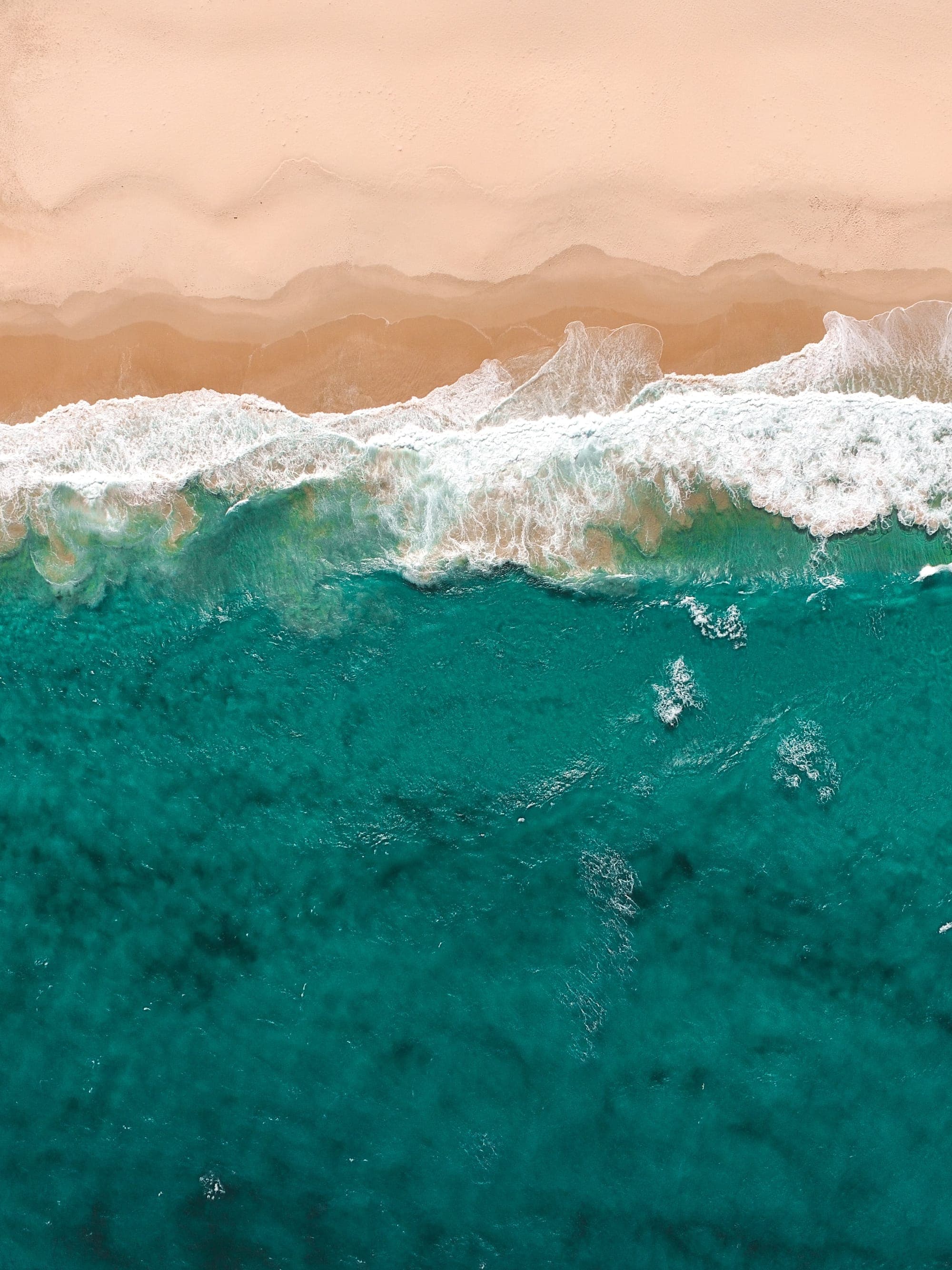 Aerial view of turquoise surf breaking along a shoreline