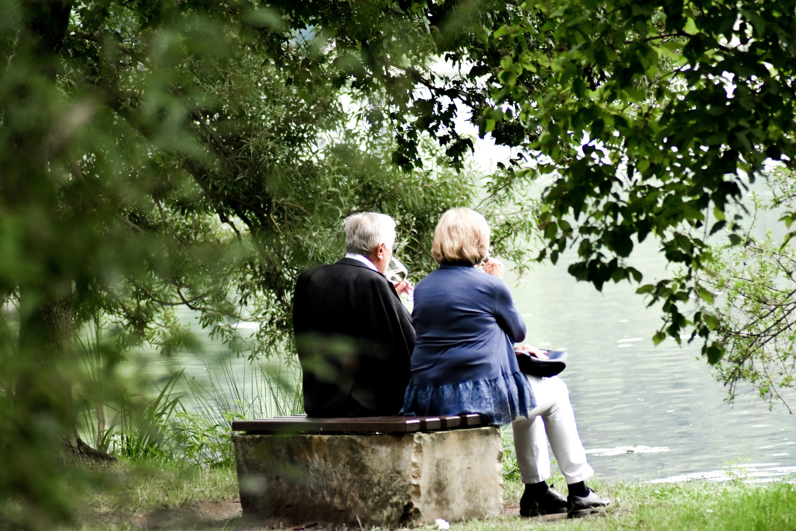senior man and women sitting together on a bench near the lake